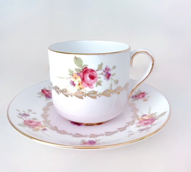 Close up of floral demitasse cup and saucer. Cup rests gently in saucer. White background.