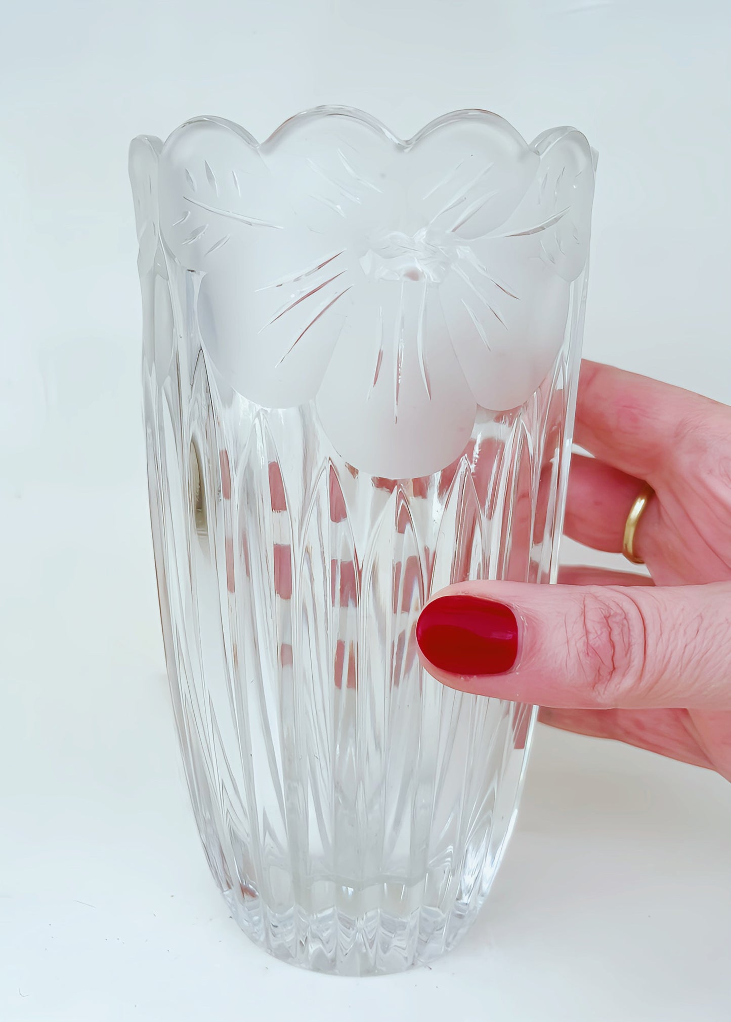Close up of vase displaying etched flower motif along brim. Held in hand. White background.