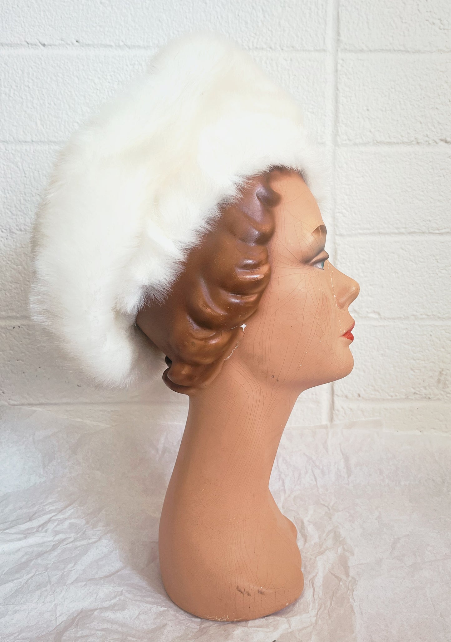 Side view image of vintage mannequin head wearing white hat with white background.
