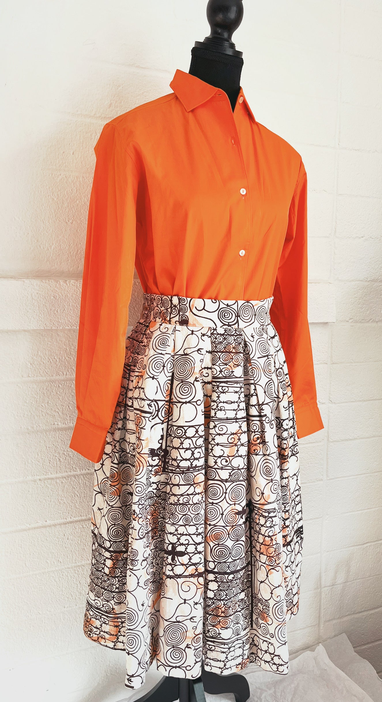 Angled image of skirt modelled on dressform with orange blouse. White background.