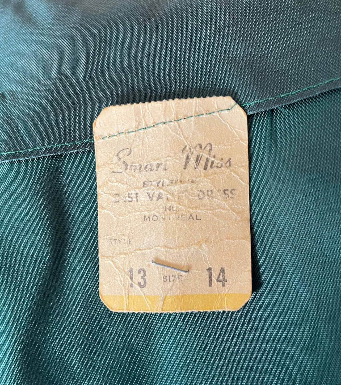 Close up uof tag pinned inside jacket. Tag reads "Smart Miss styles. Best Value Dress. Montreal. Size 13 14."