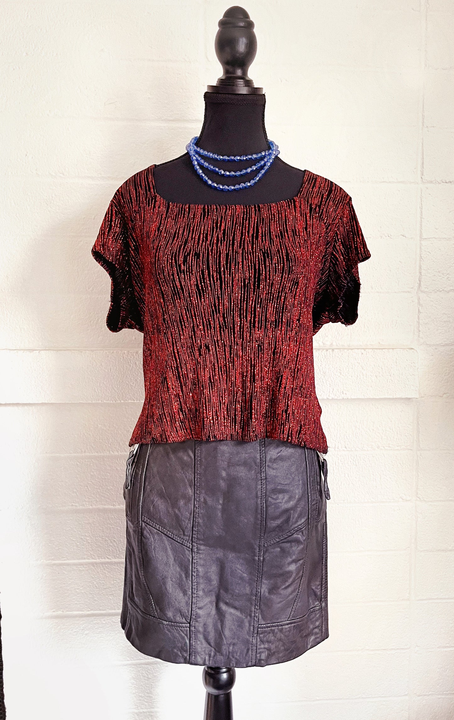 Image of skirt modelled on dressform with sparkly red top and blue necklace. White background.