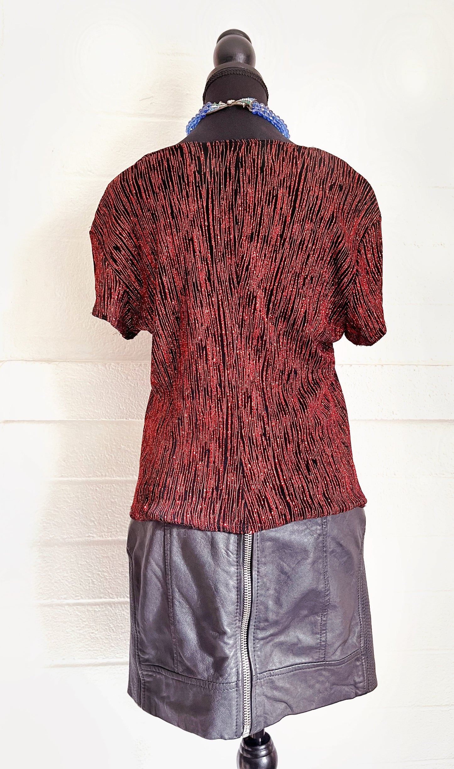 Backside image of skirt modelled on dressform with sparkly red top and blue necklace. White background.