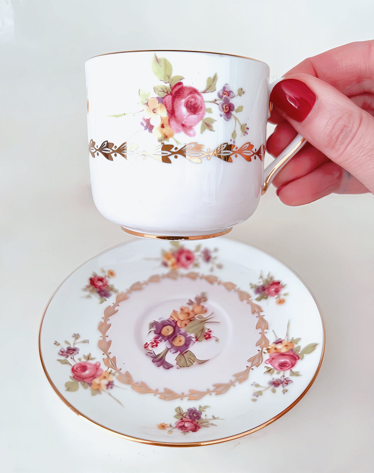 Close up of cup being held by handle.  Saucer in background.  White background