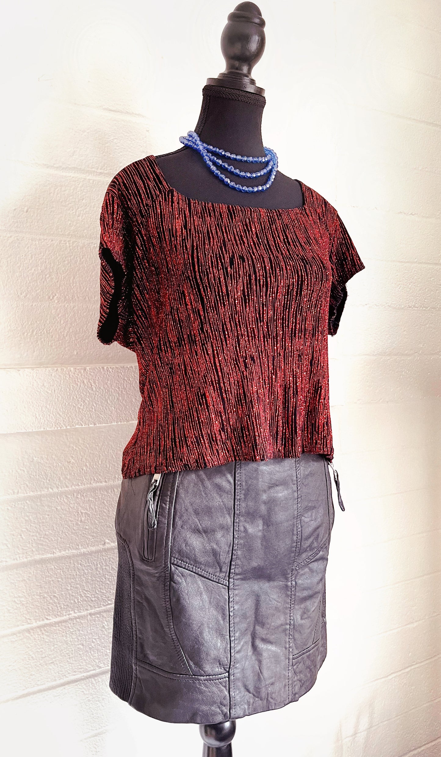 Image of skirt modelled on dressform with sparkly red top and blue necklace.  White background.  